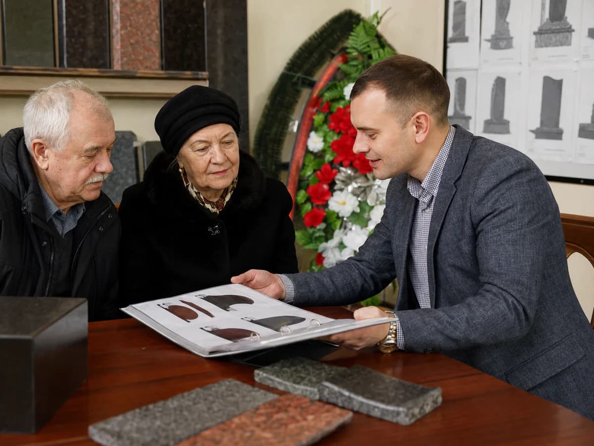 Консультант мастерской помогает выбрать памятник по каталогу эскизов